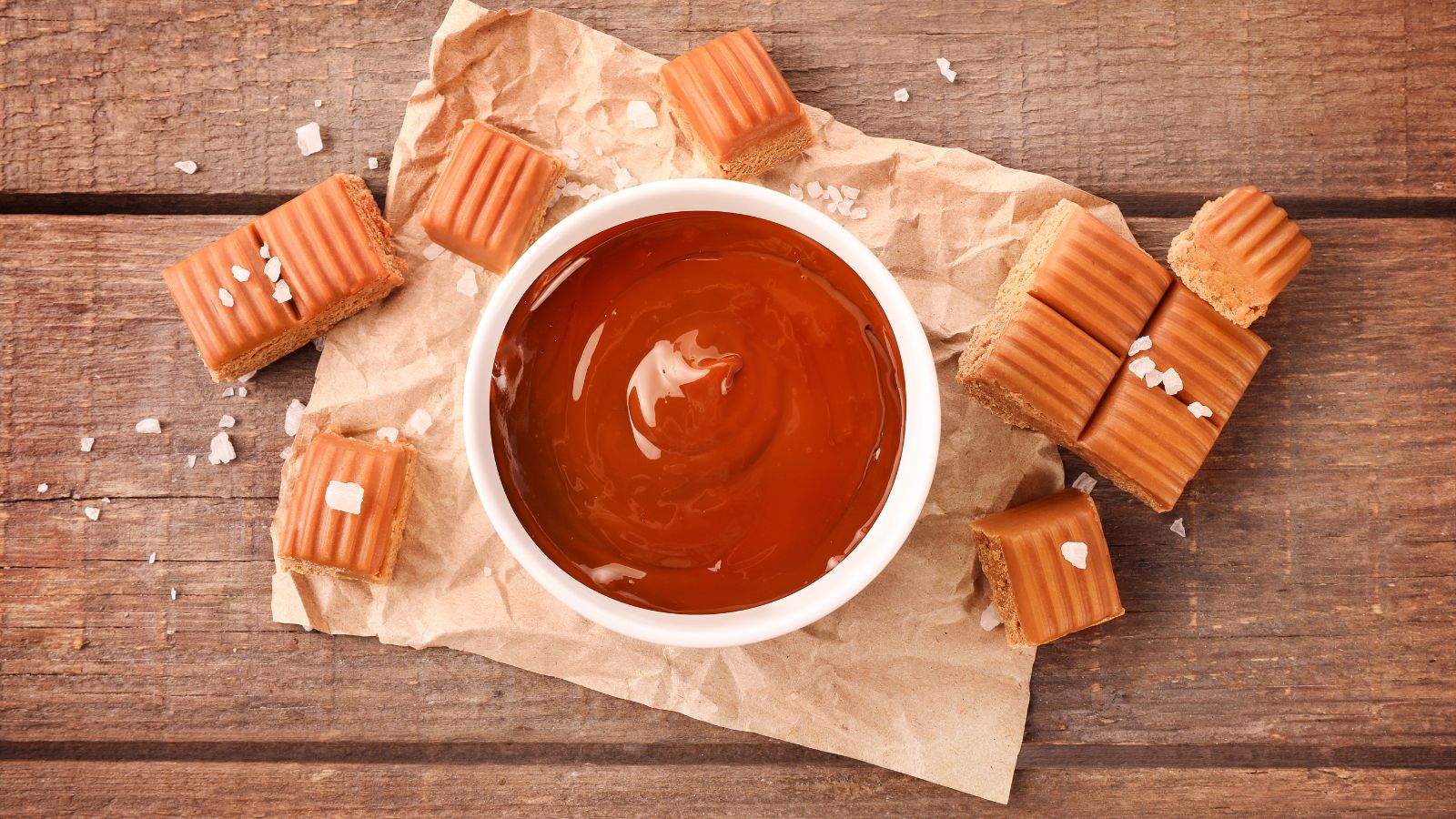 Bowl of caramel sauce with salted caramel fudge on paper wrap.