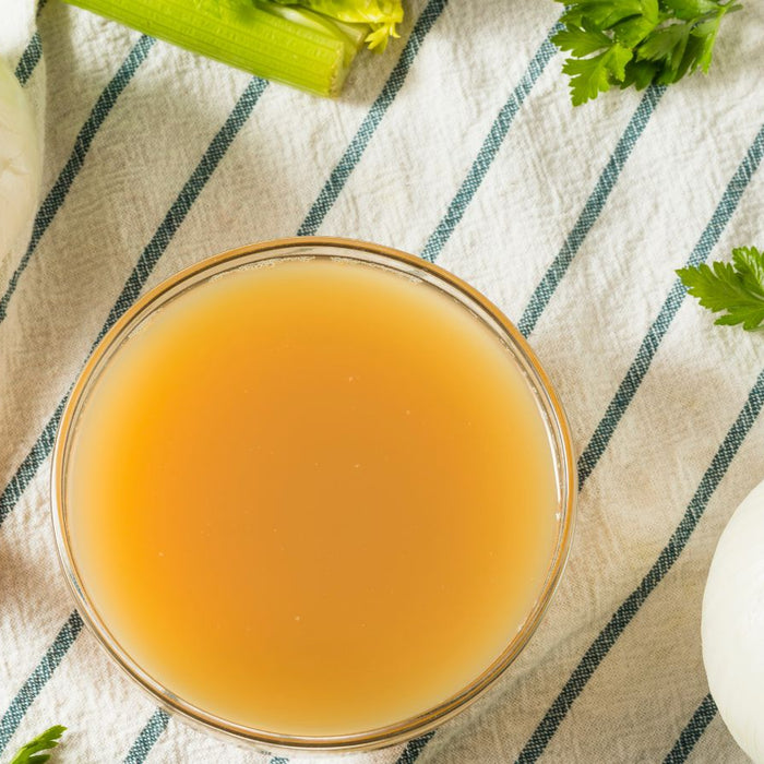 Bowl of vegetable broth with onions, carrots, and celery on a towel.