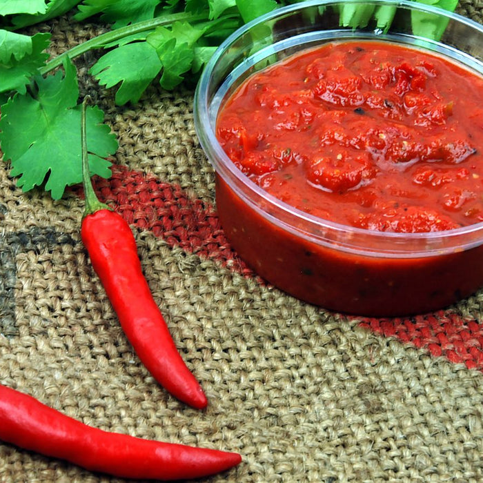 Salsa in plastic container with fresh chilies and herbs.