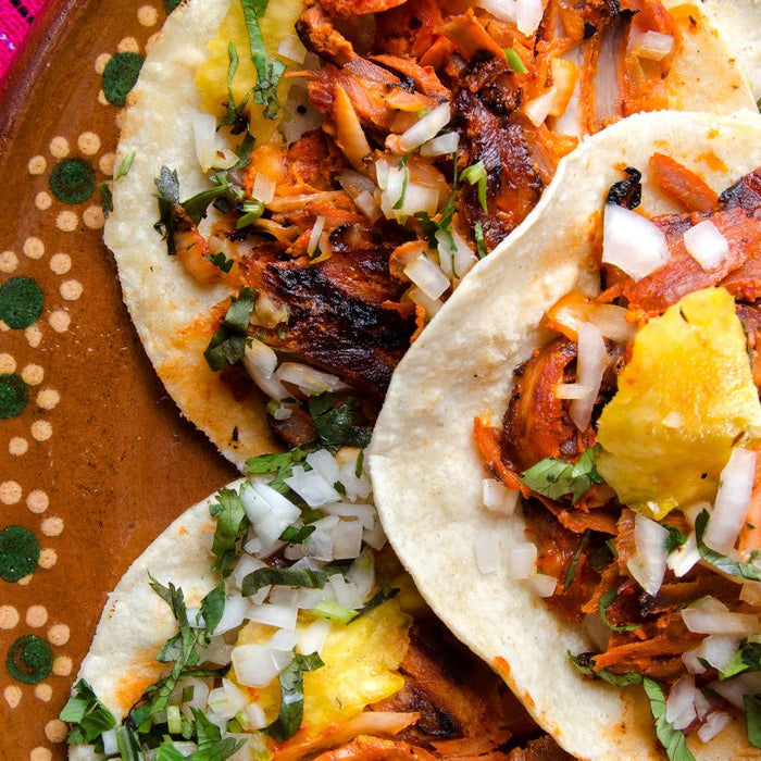 Tacos al pastor with pineapple, onion, and cilantro on a clay plate.