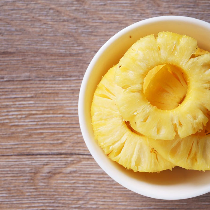 Bowl of fresh pineapple rings on a wooden surface.