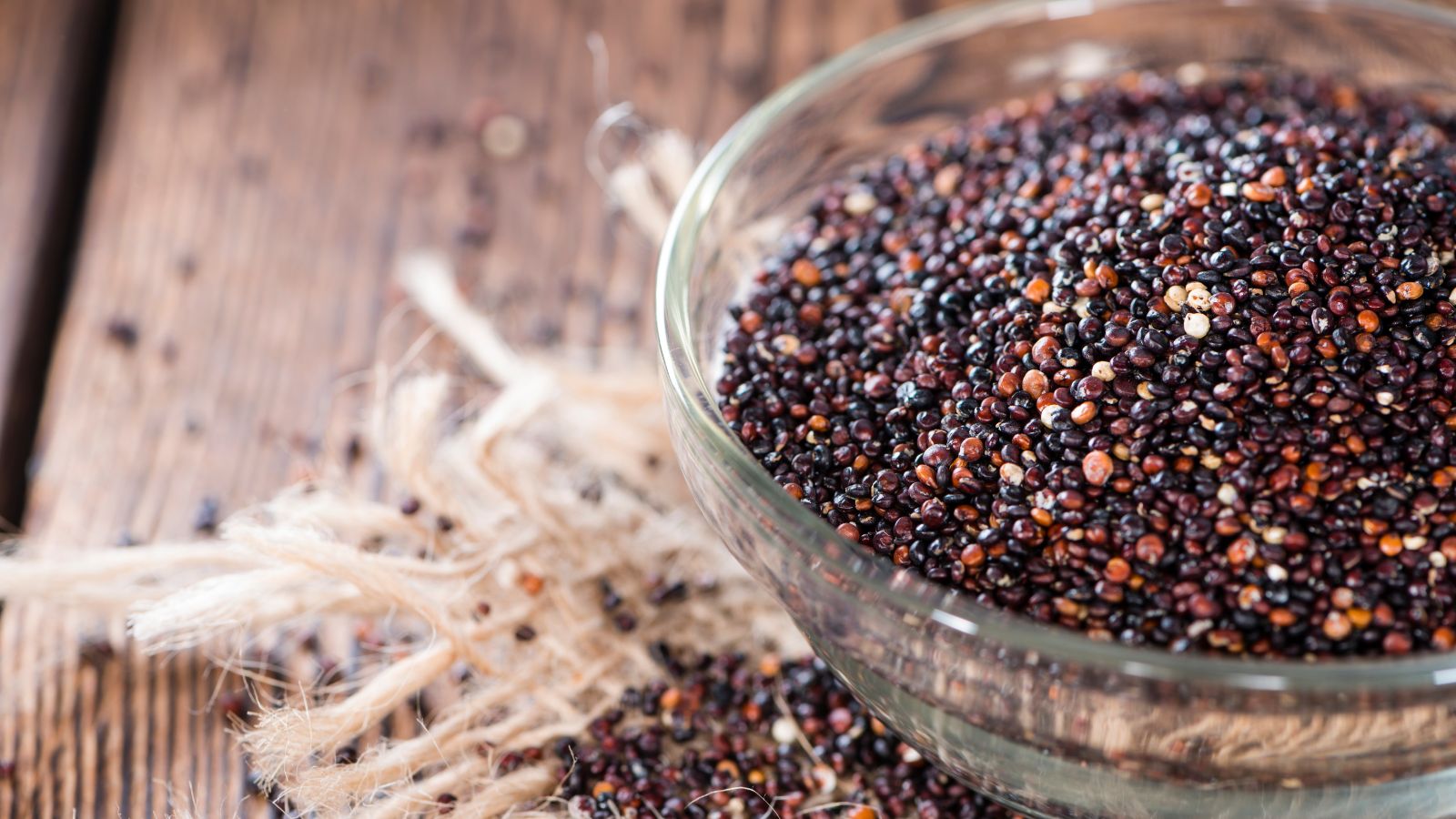 Glass bowl filled with black quinoa on a rustic wooden surface.