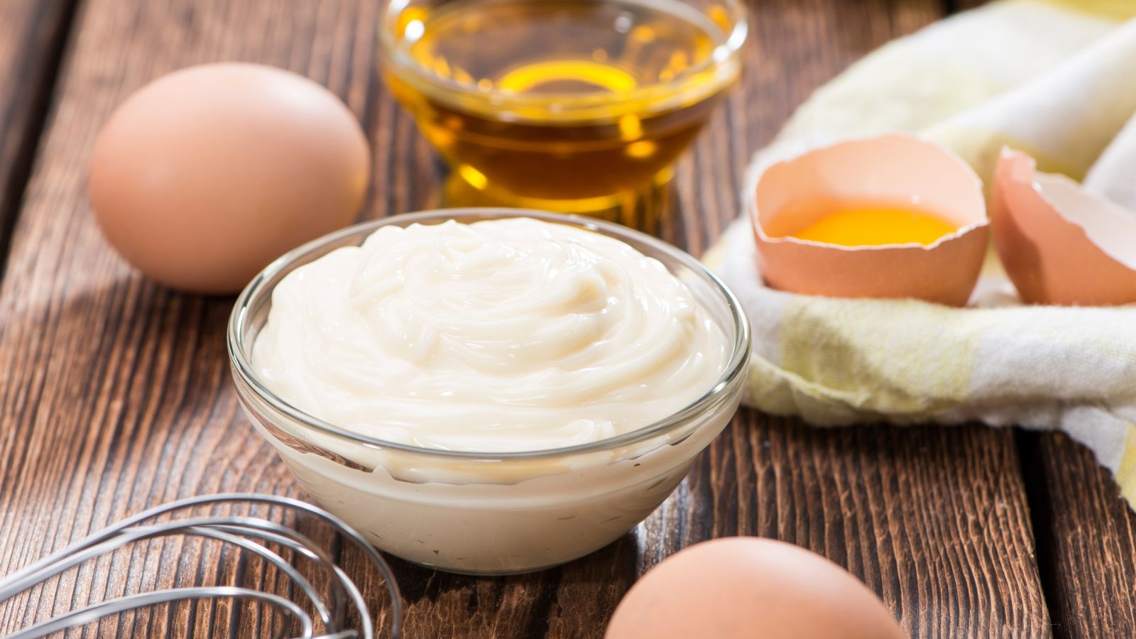 Fresh creamy mayo in glass bowl with eggs and oil on table.