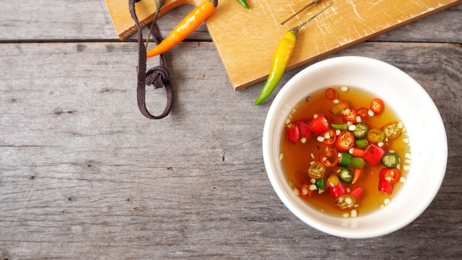 Chili fish sauce in white bowl on wooden table with peppers on side.
