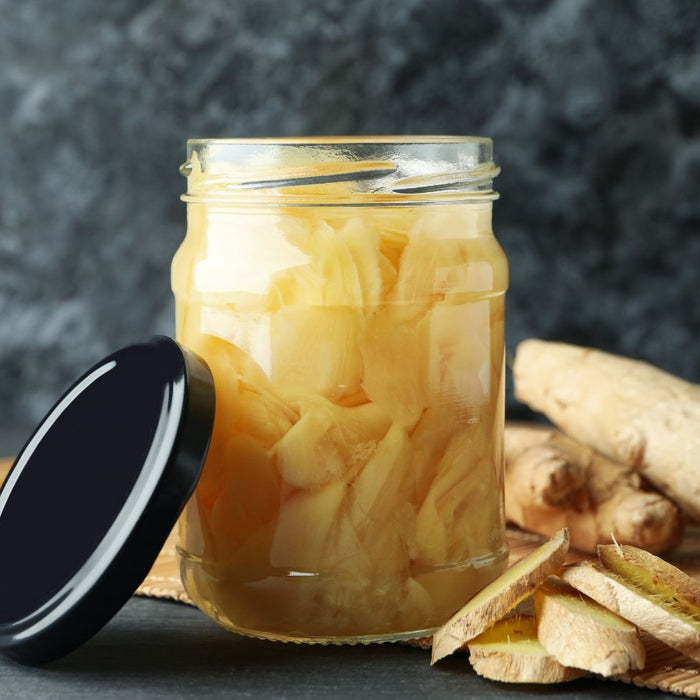 Pickled ginger slices in glass jar with fresh root on bamboo mat