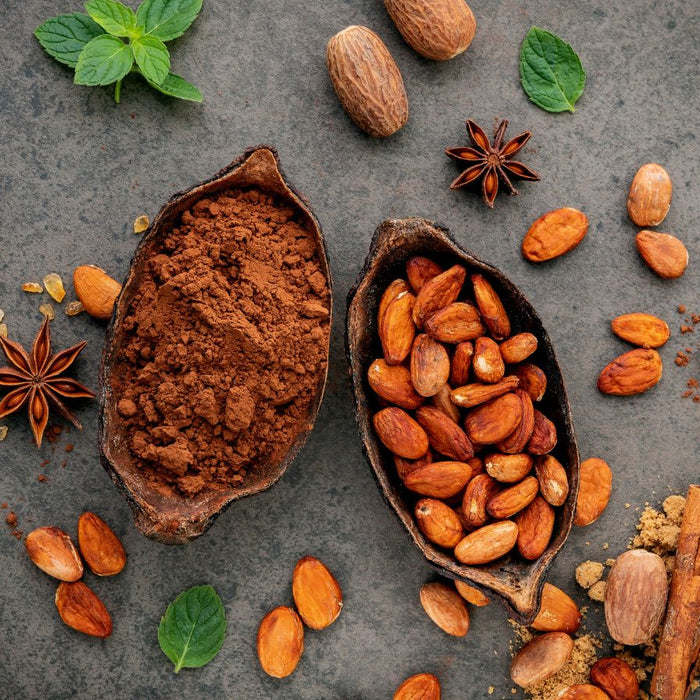 Cocoa powder and roasted cacao beans with spices on a rustic surface.