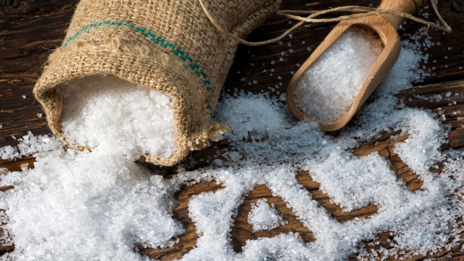 Coarse sea salt spilling from a burlap sack onto a wooden surface