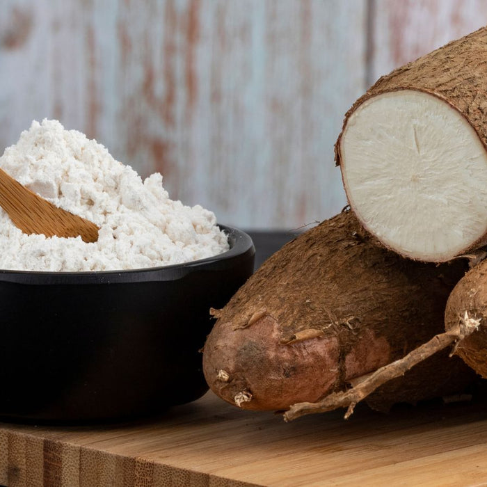 Bowl of tapioca flour and whole cassava roots on wooden board.