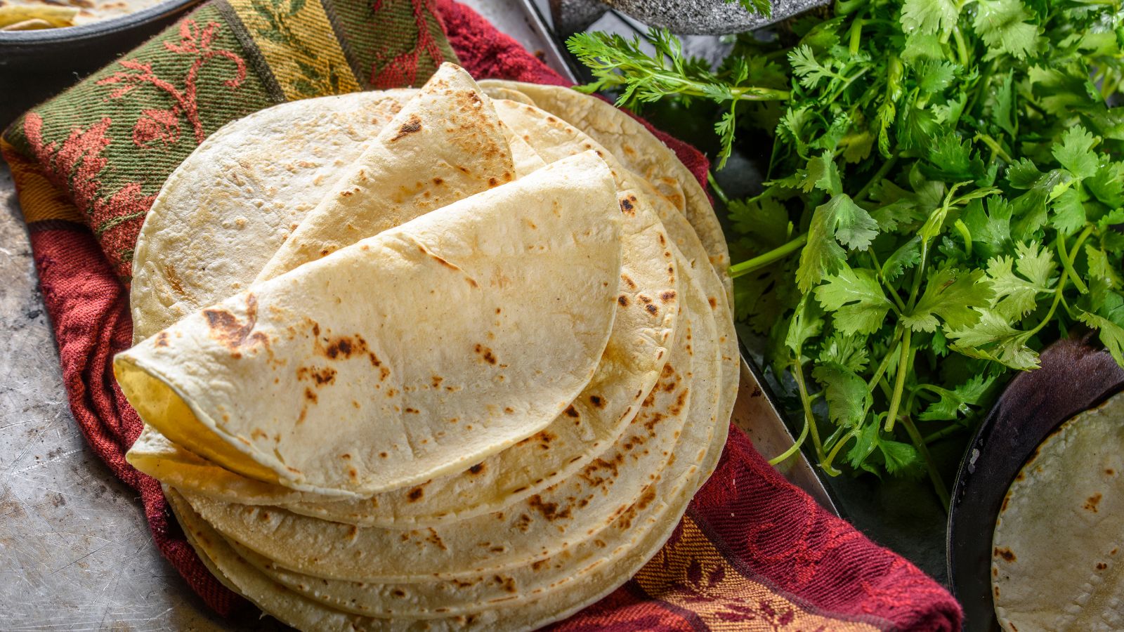 Freshly made flour tortillas stacked on a colorful kitchen towel