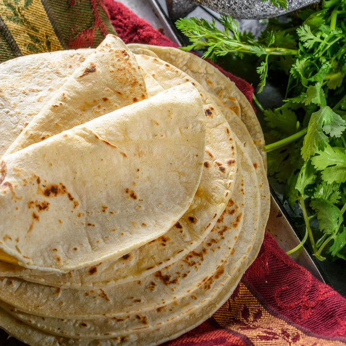 Freshly made flour tortillas stacked on a colorful kitchen towel