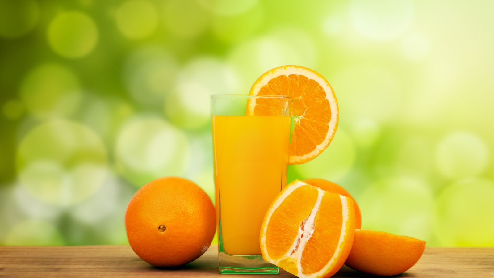 Fresh orange juice with whole and sliced oranges on wooden table.