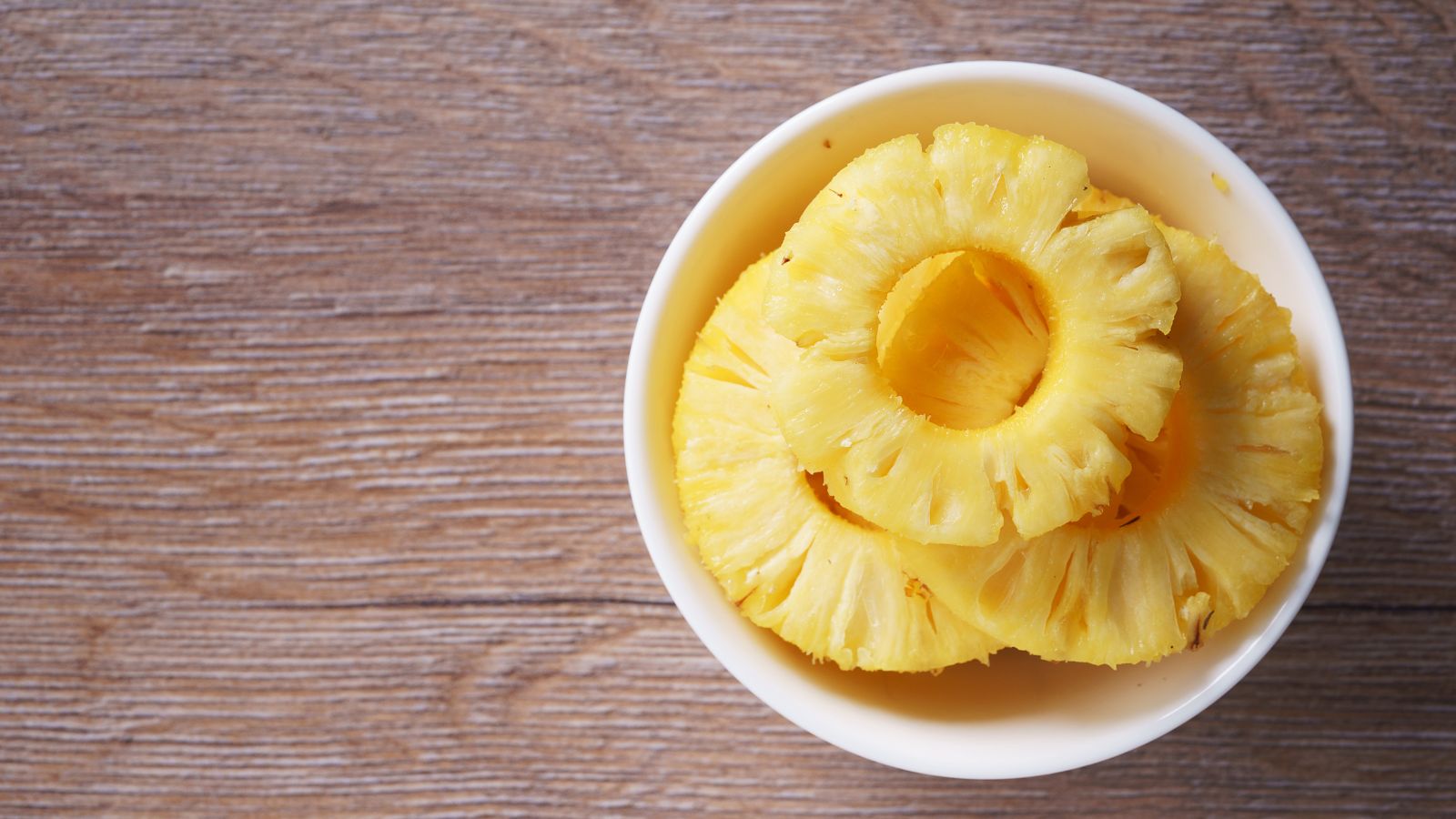 Bowl of fresh pineapple rings on a wooden surface.