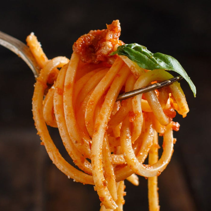 Fork holding spaghetti with marinara sauce and basil leaf close-up
