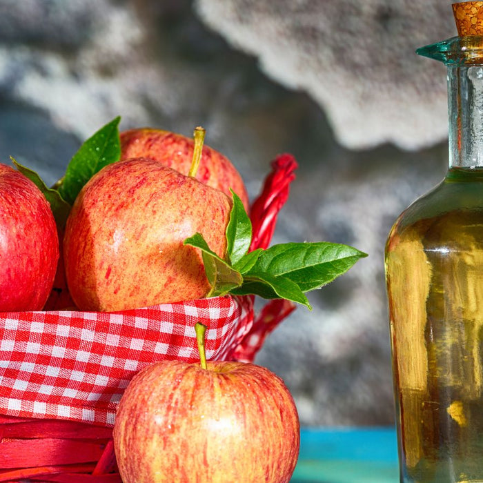 Fresh red apples in a basket with apple cider vinegar bottle beside