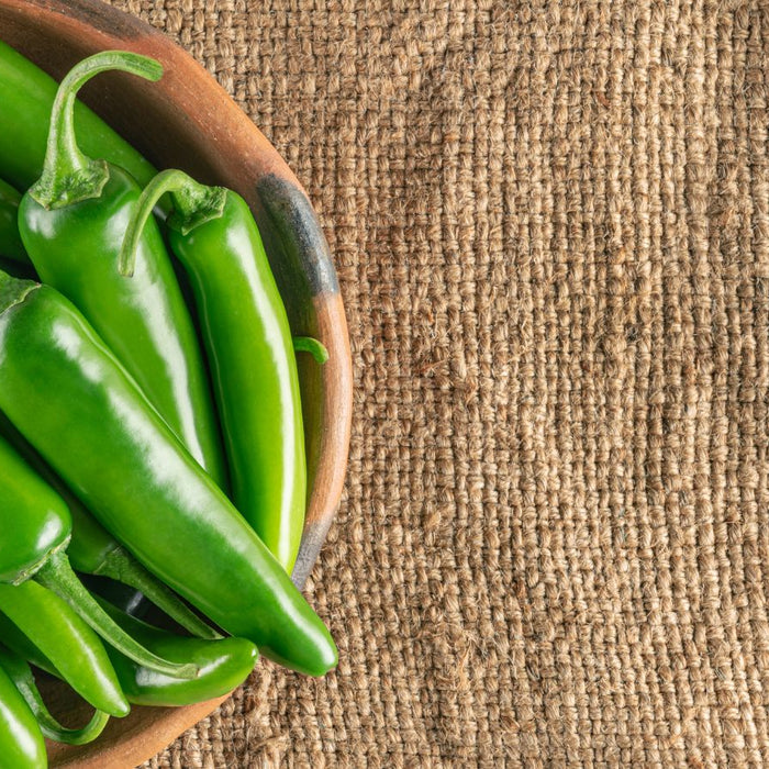 Fresh green jalapeno peppers in wooden bowl on burlap background
