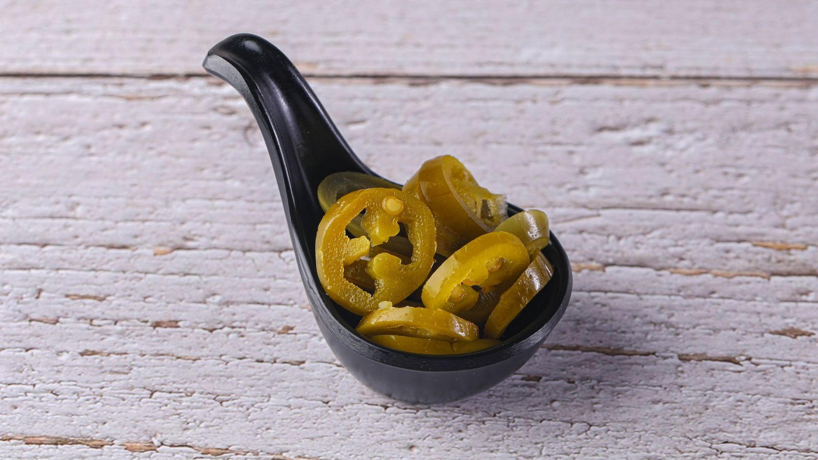 Bowl of sliced pickled jalapeños on rustic white surface