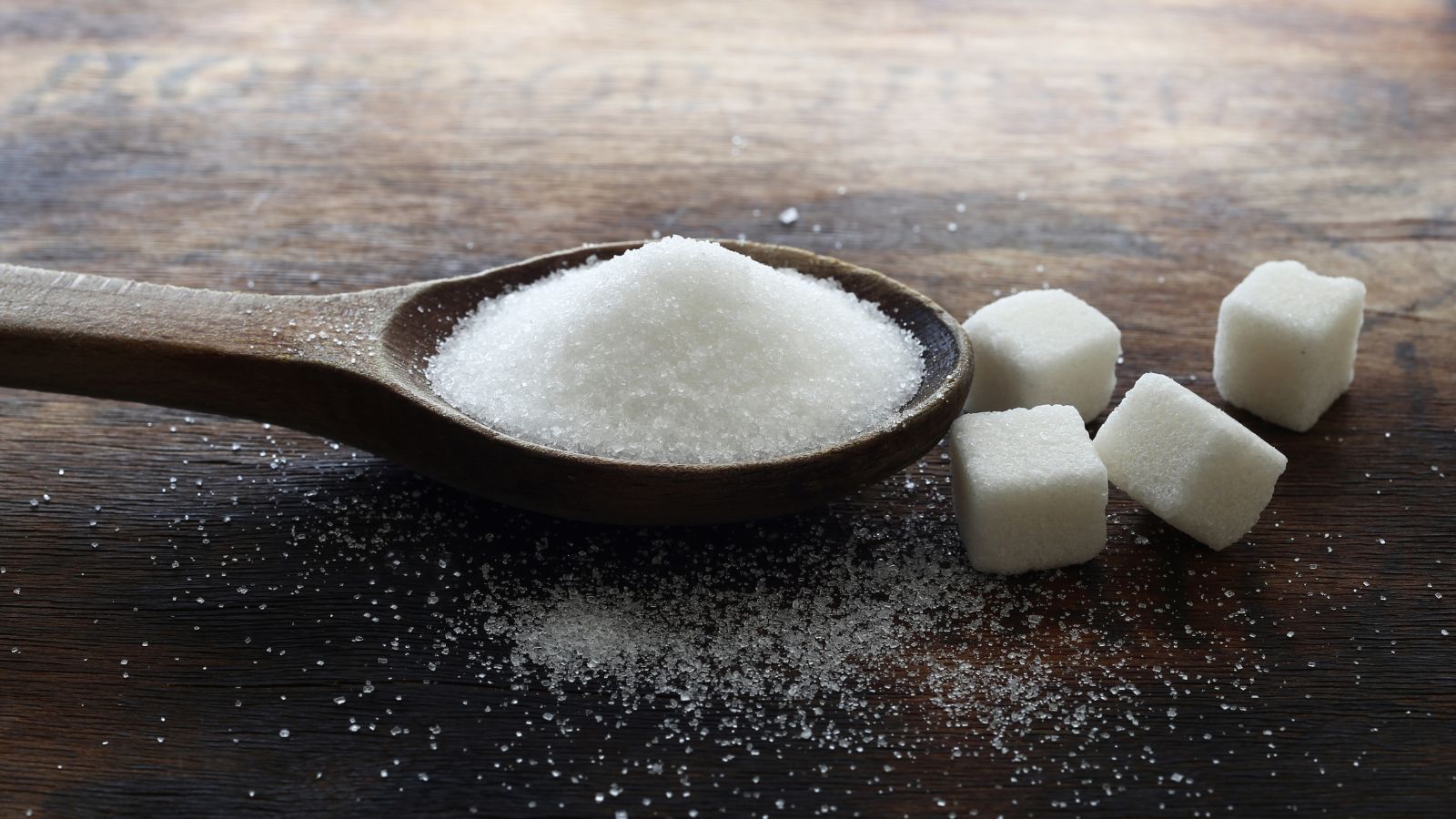 White sugar on wooden spoon with sugar cubes on rustic table.