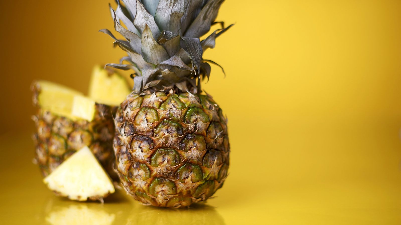 Whole pineapple with slices on yellow background.