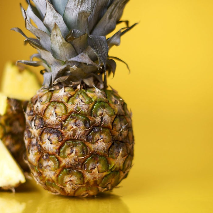 Whole pineapple with slices on yellow background.