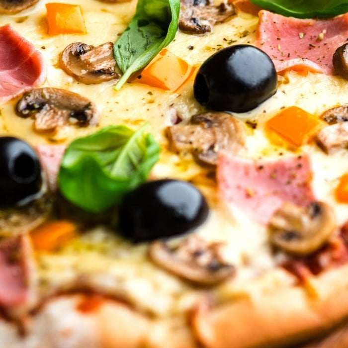 Pizza with olives, mushrooms, ham, cheese, and fresh basil leaves.