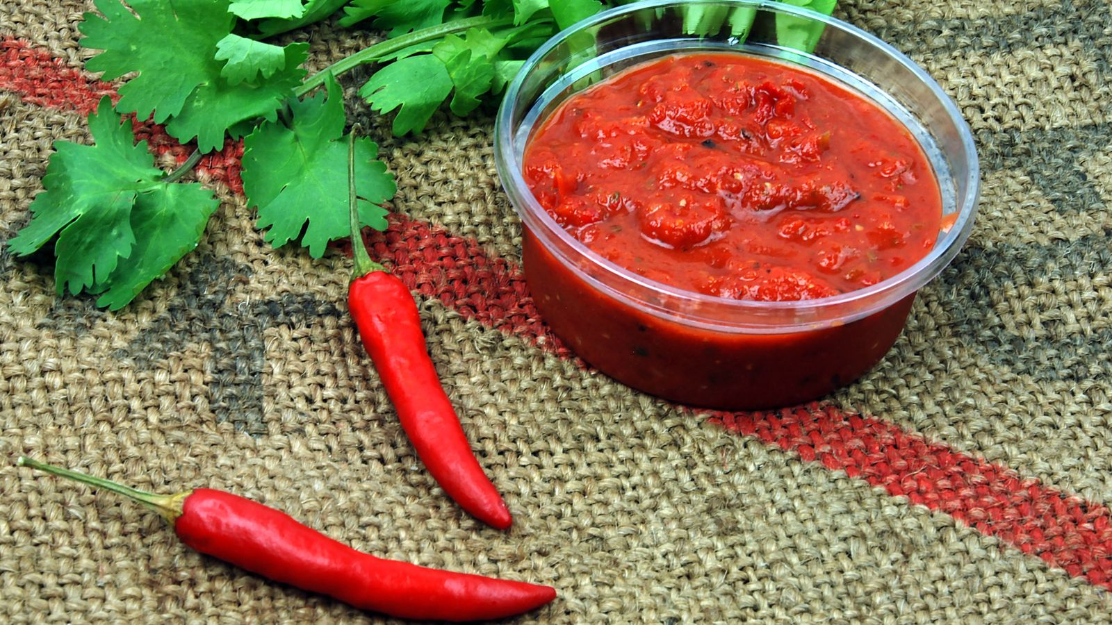 Salsa in plastic container with fresh chilies and herbs.