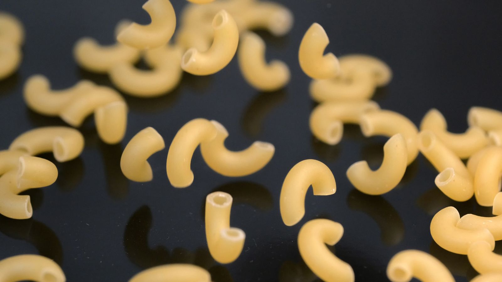 Uncooked elbow macaroni pasta scattered on black surface.