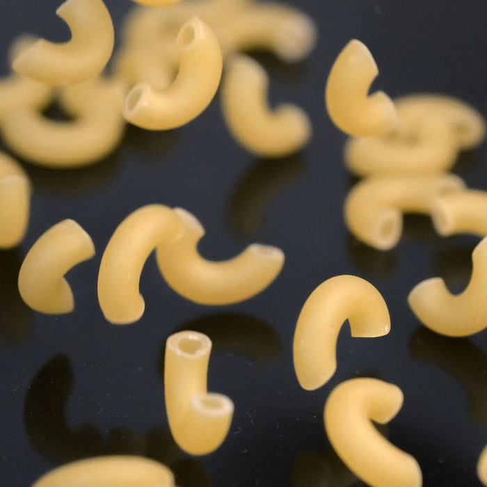Uncooked elbow macaroni pasta scattered on black surface.