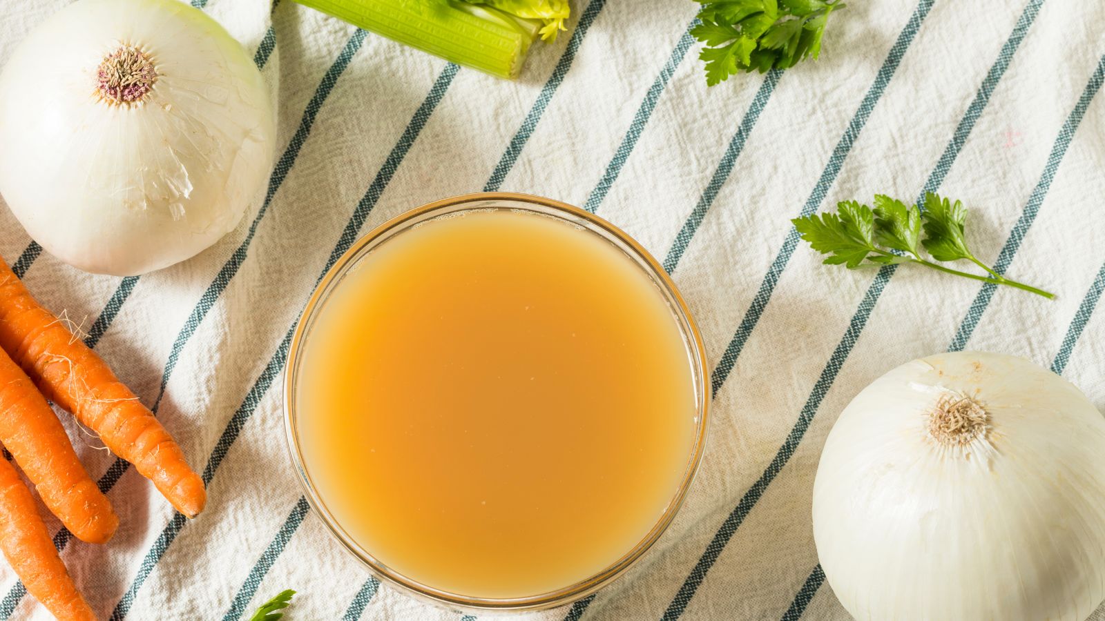 Bowl of vegetable broth with onions, carrots, and celery on a towel.