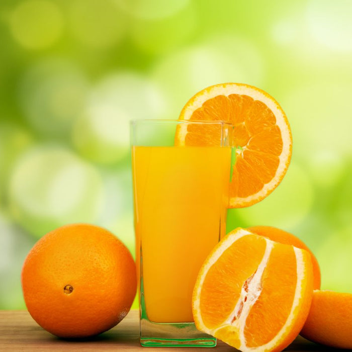 Fresh orange juice with whole and sliced oranges on wooden table.