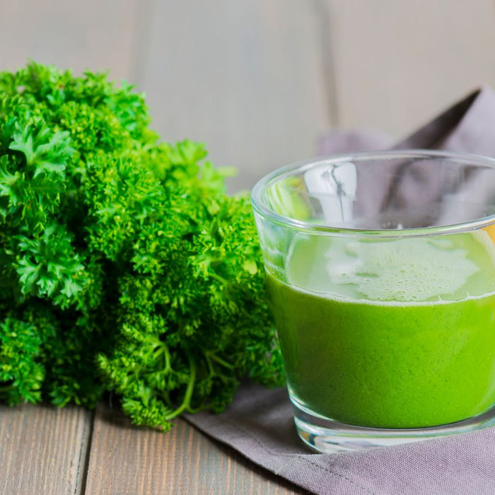 Glass of green juice with parsley and lemon on rustic table.