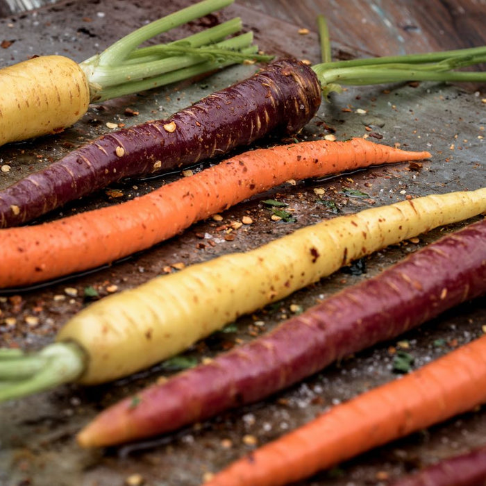 Seasoned heirloom carrots in purple, orange, and yellow on baking sheet.