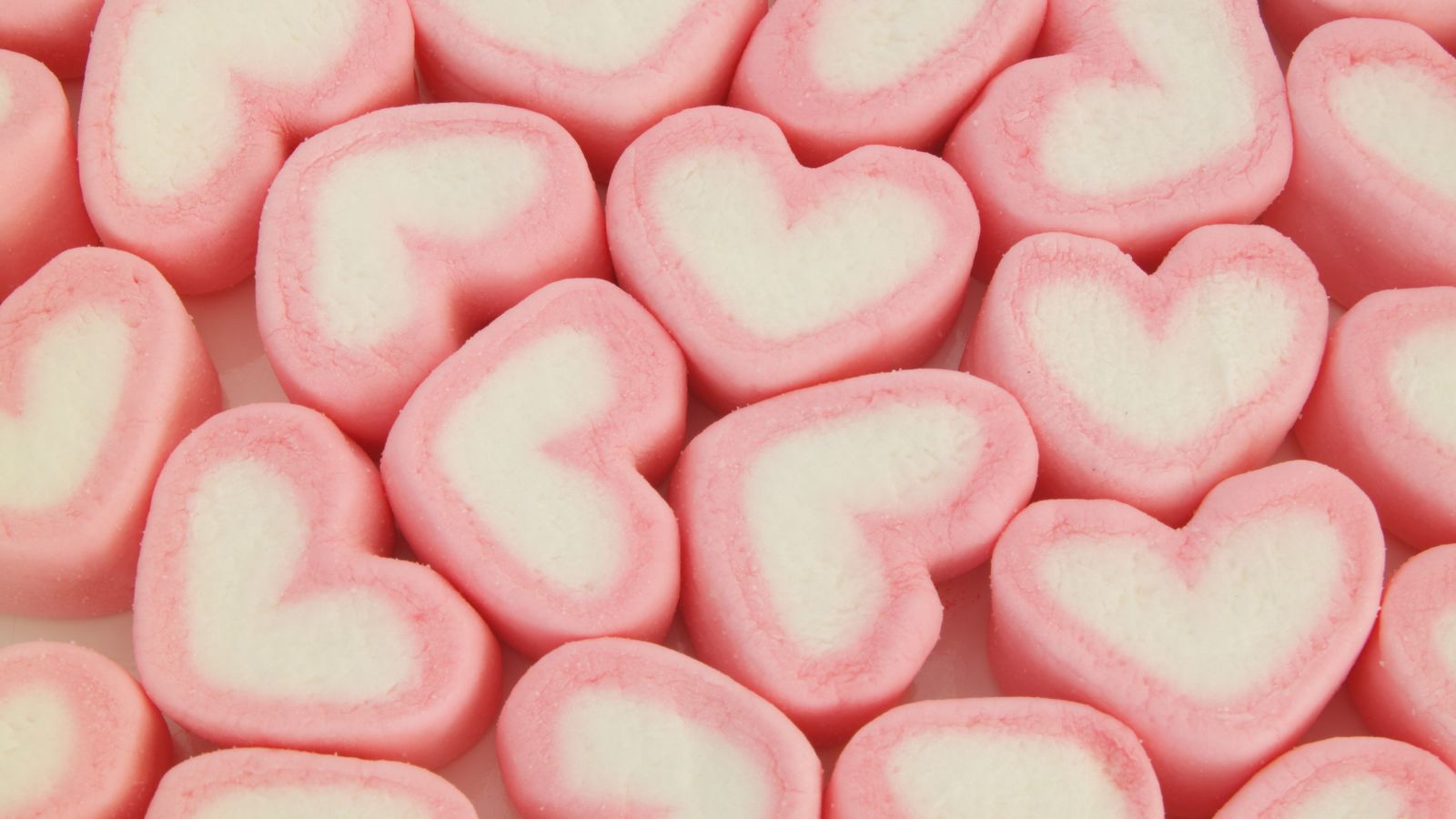 Heart-shaped pink and white candies with a soft texture, arranged closely together.