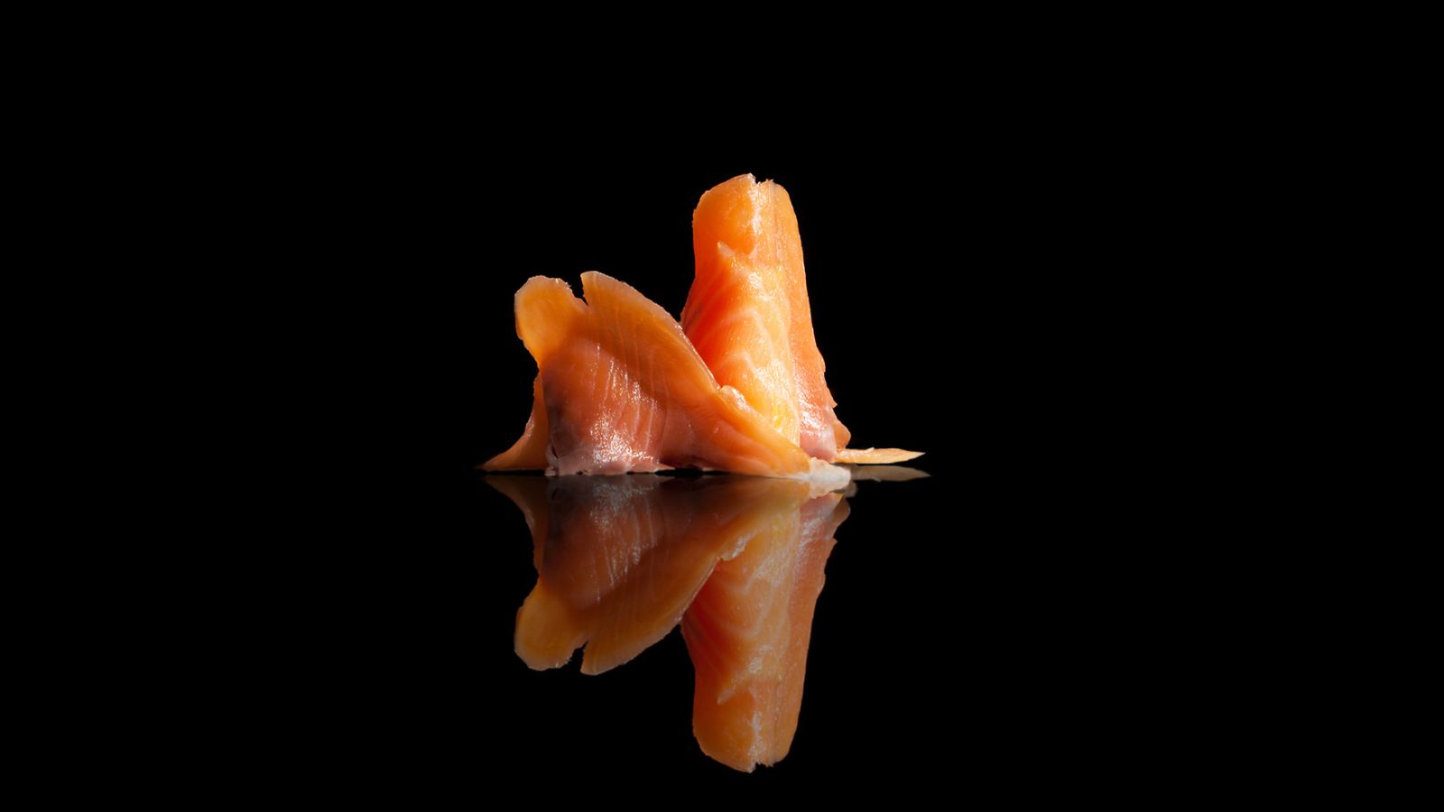 Thin slices of smoked salmon with reflection on black surface.