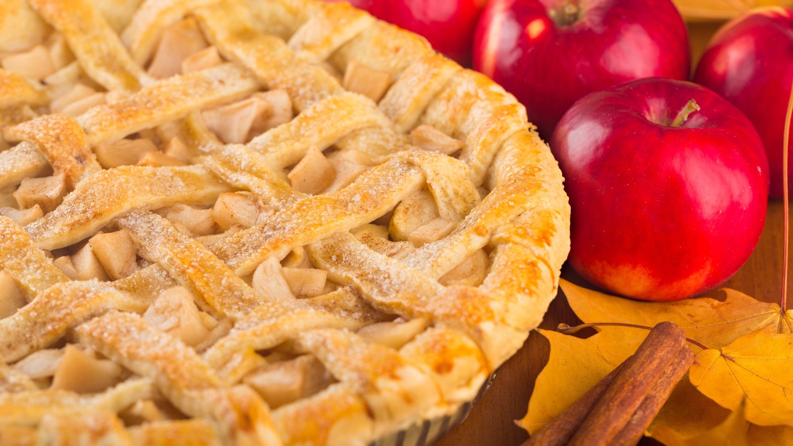 Homemade apple pie with cinnamon sticks and red apples on the table