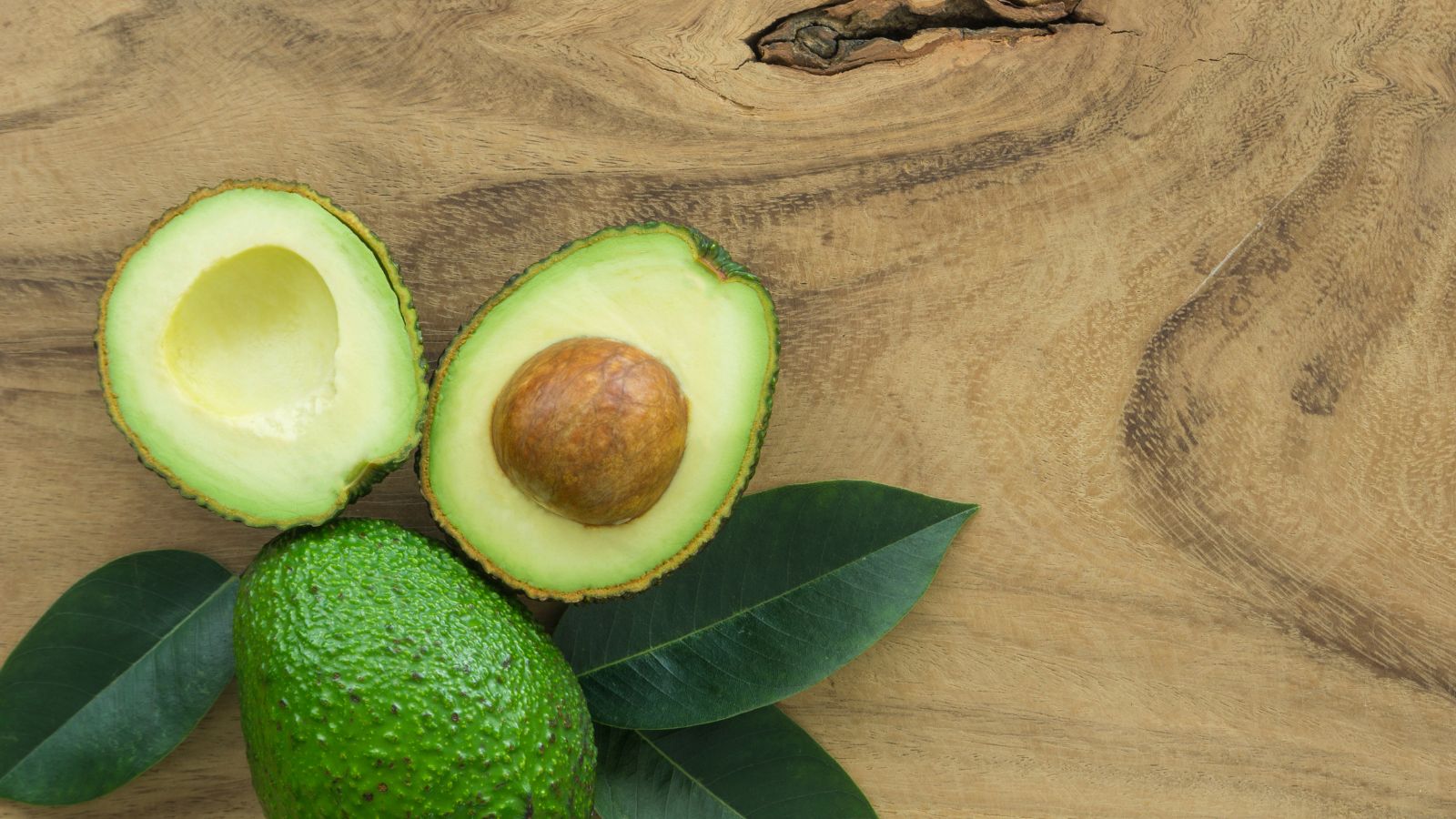 Fresh avocado halves with seed and leaves on wooden background