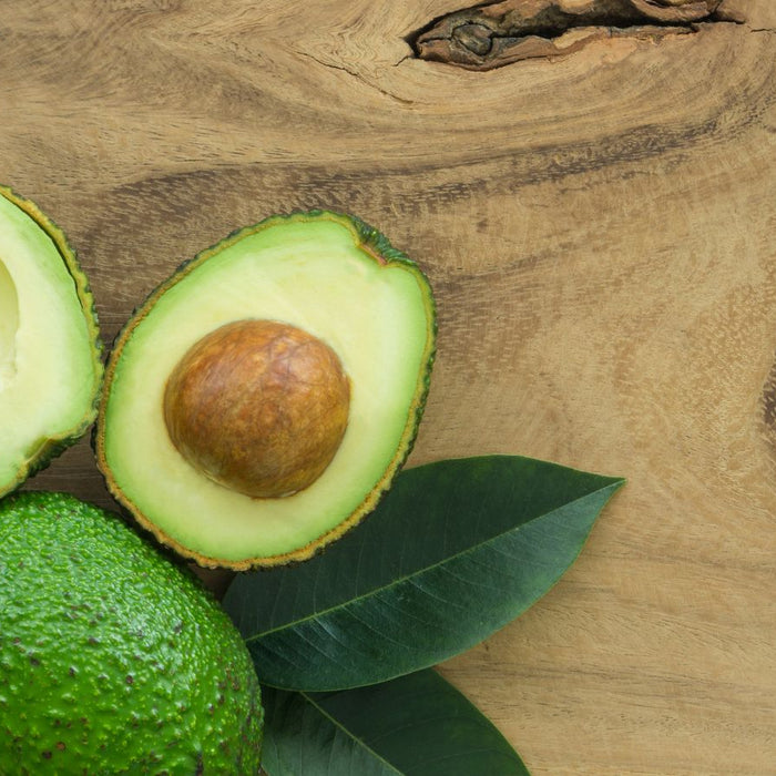 Fresh avocado halves with seed and leaves on wooden background