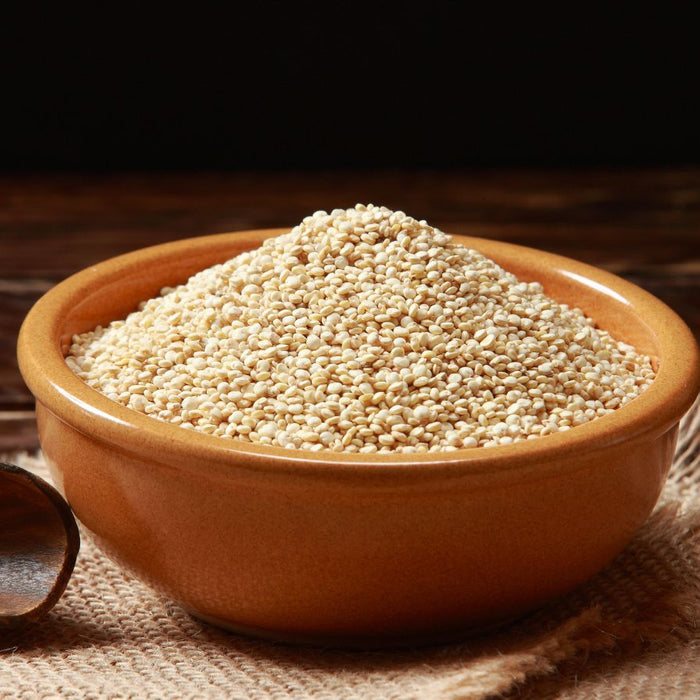 Bowl of dry white quinoa seeds on wooden table.