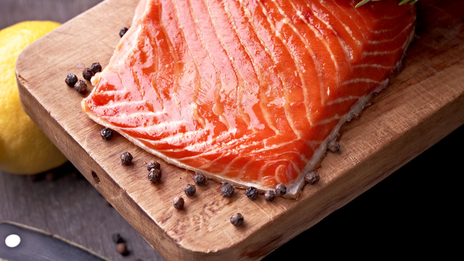 Fresh salmon fillet on a wooden board with peppercorns.