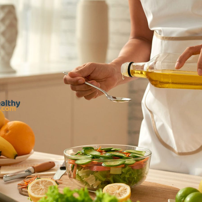 Person pouring olive oil into spoon to make fresh vegetable salad.