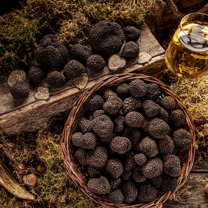 Assorted black truffles in basket and on board with wine glass.