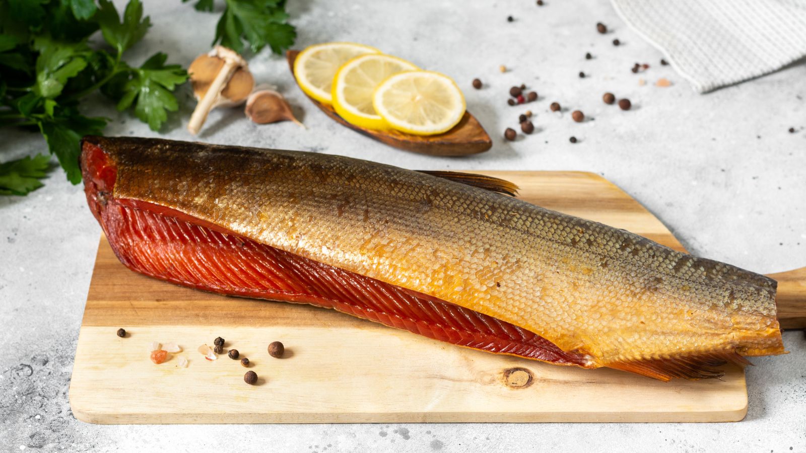 Smoked salmon fillet on cutting board with spices and herbs.
