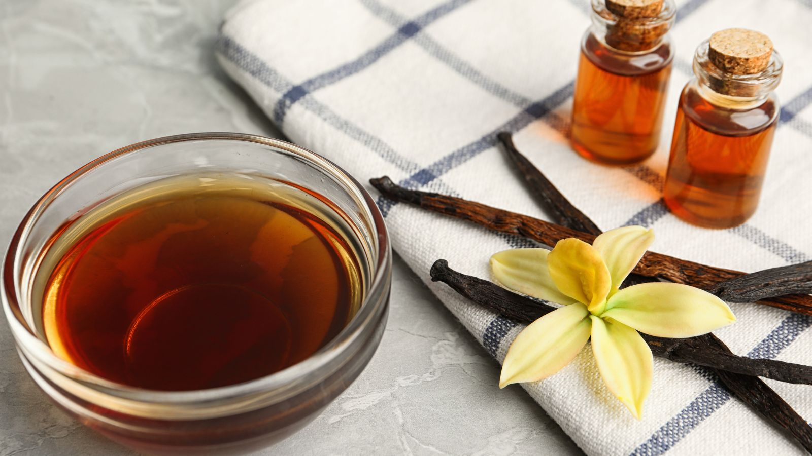 Vanilla extract with pods and flower on cloth.