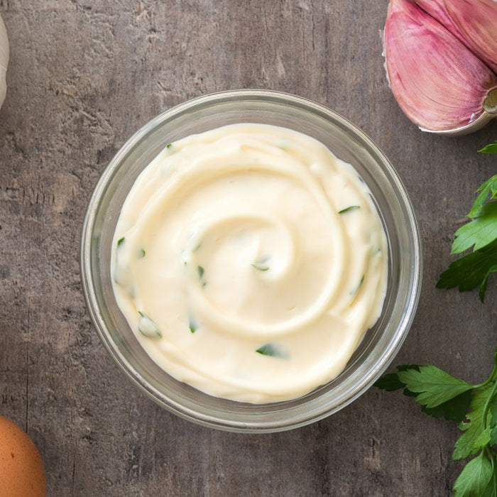 Garlic mayo sauce with herbs, eggs, garlic, and parsley on wood.