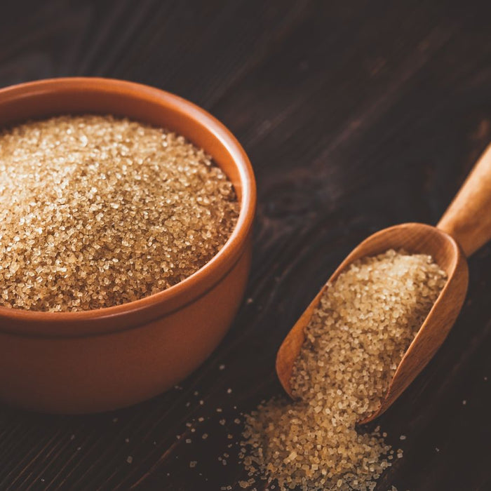 Raw brown sugar in bowl with wooden scoop on dark table.