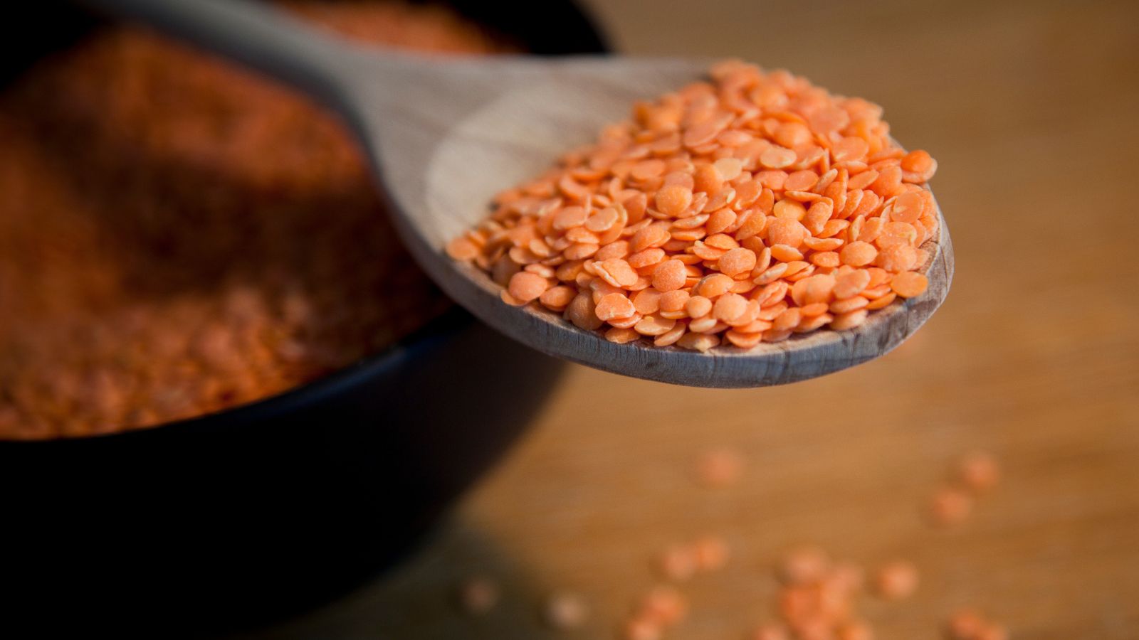 Close-up of red lentils on wooden spoon above black bowl