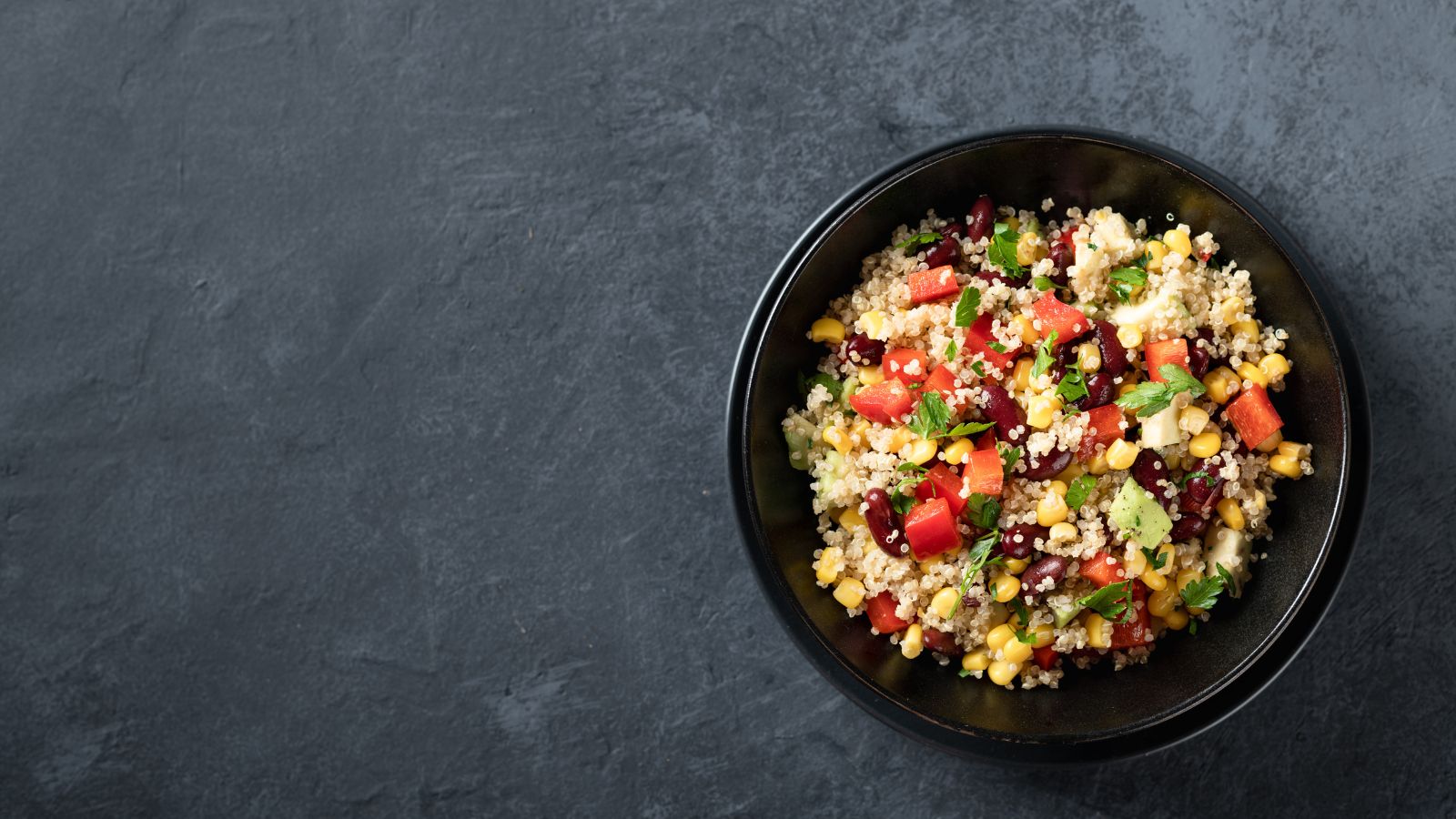 Quinoa salad with vegetables and herbs in a black bowl on a dark background.