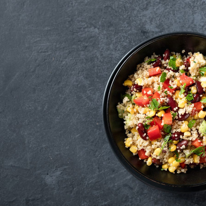 Quinoa salad with vegetables and herbs in a black bowl on a dark background.