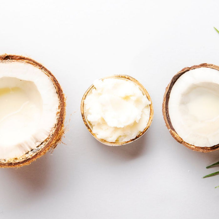 Halved coconuts with coconut oil and milk arranged on a white surface.