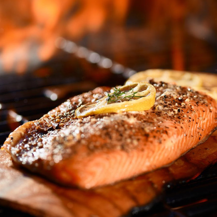 Cooked salmon fillet with lemon slices on cedar plank.
