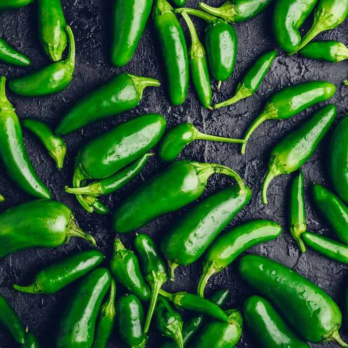 Pile of fresh jalapeno peppers spread on dark textured surface
